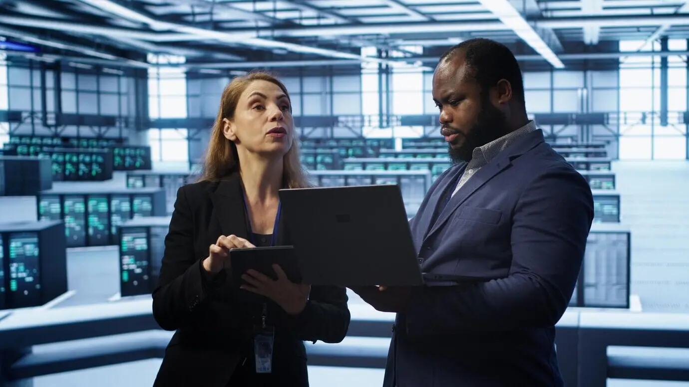 Руководитель в серверной ферме контролирует работу инженера, устраняющего сетевые неполадки.